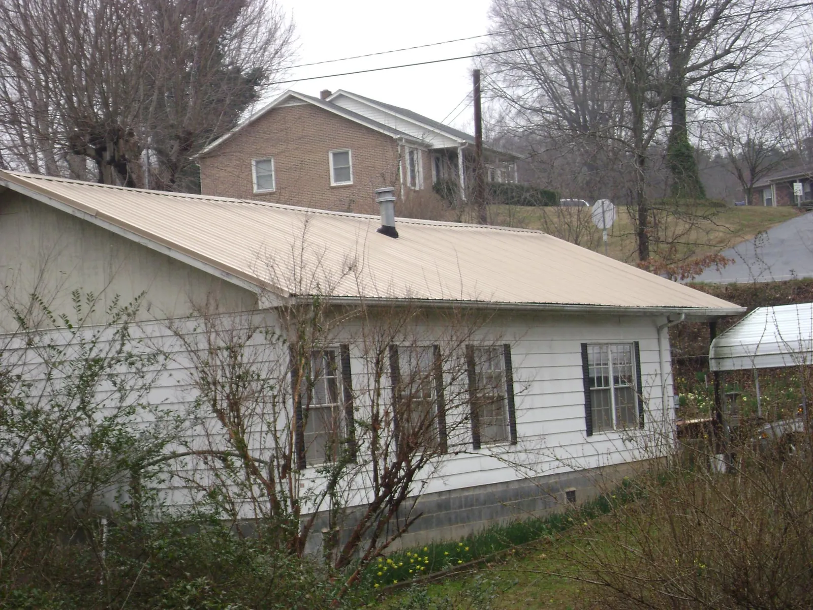 Tan metal roof on a white sided house set into a hillside — Commercial Roofing by Roofing Brothers in Carlton